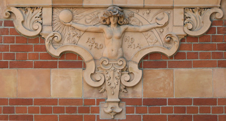 terracotta sculpture on exterior of red-brick building, shows a figure with outstretched arms, holding sun and moon