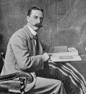 old black and white photo of Edwardian gentleman, moustache, seated at desk, turning to look at viewer