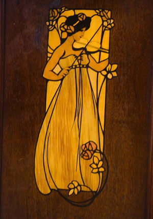 inlay to a wooden cabinet shows a tall female figure, golden in tone